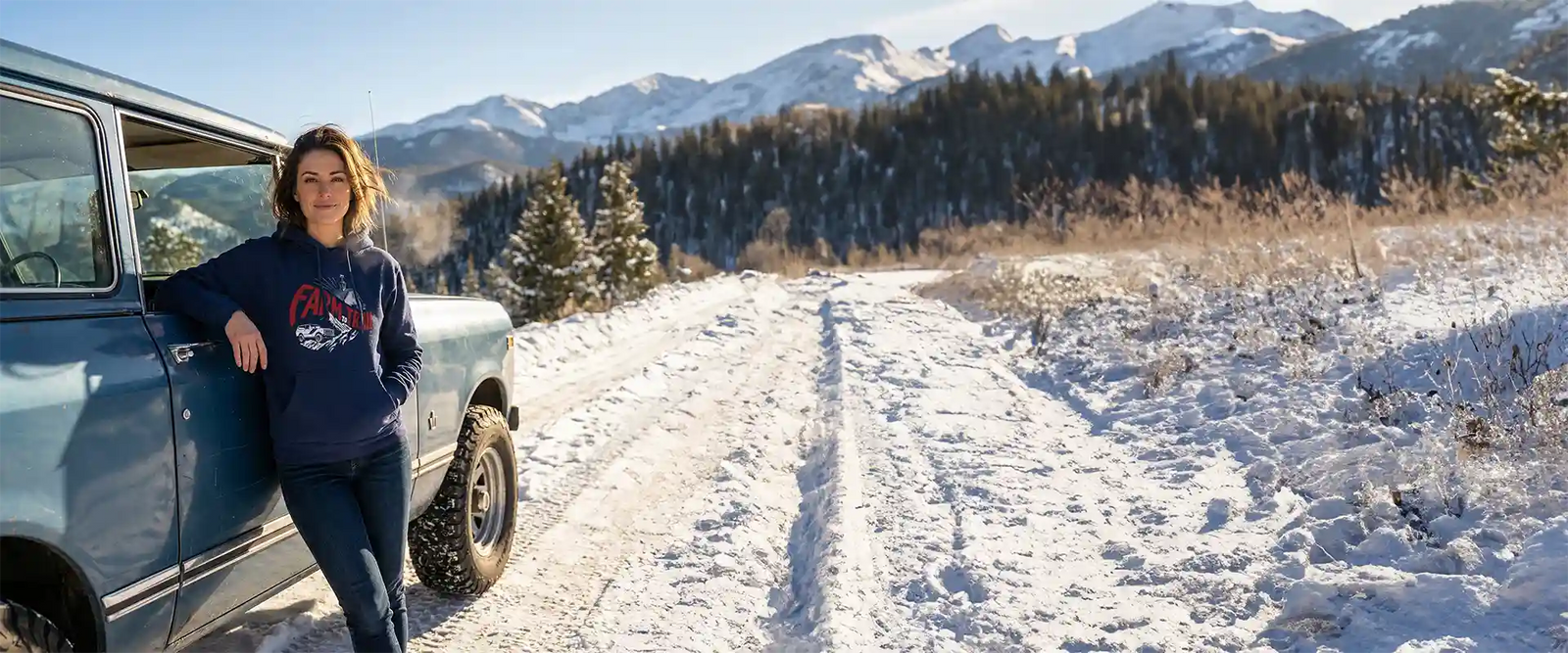 Woman wearing Farm to Trail sweatshirt leaning against an International Scout
