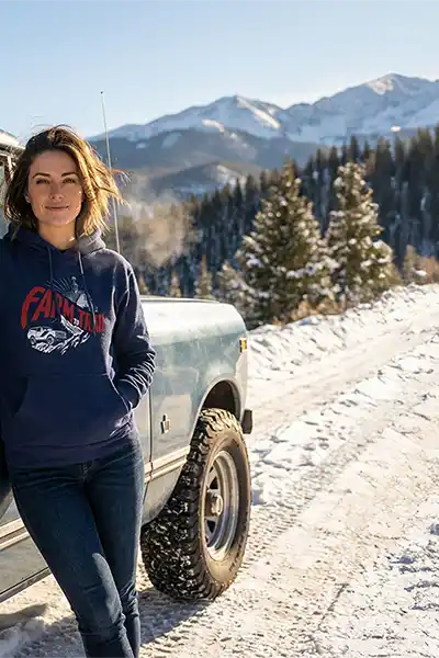 Girl wearing Farm to Trail hoodie standing next to a vintage Scout on winter road